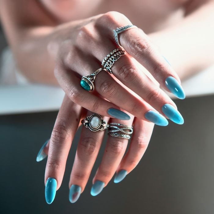 Close-up of hands with long manicured blue nails adorned with silver rings.