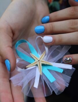 Hands with colorful nails holding a starfish-decorated accessory with ribbons and tulle.