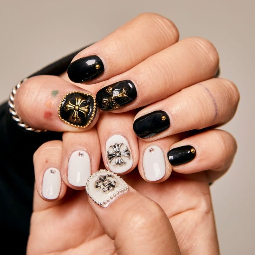 Close-up of women's hands showcasing artistic black and white nail art with ornate embellishments.