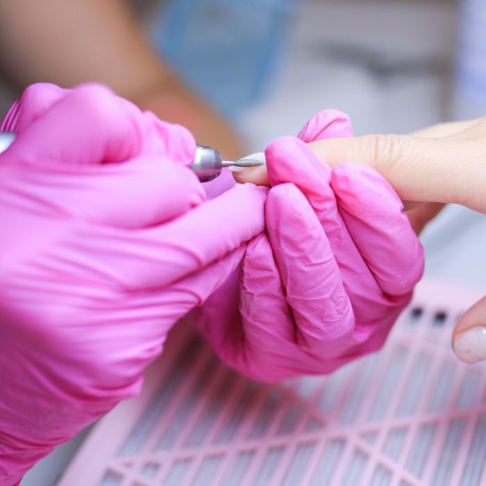 Close-up of a manicure procedure in a Polish salon with technician in pink gloves.