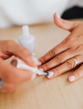 A detailed view of hands applying nail polish on natural nails with a gold ring.