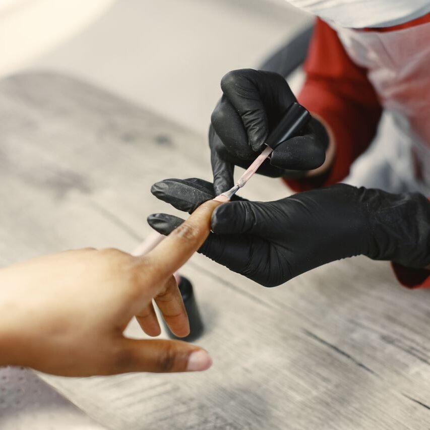 A nail artist carefully applies nail polish to a client's nails in a salon setting, using precise techniques.